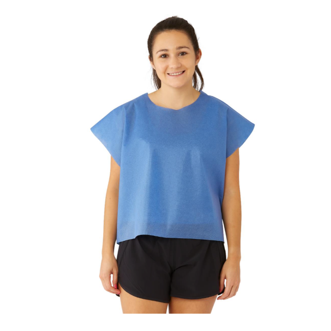 A young woman smiles while wearing a Medline Disposable Multilayer Patient Cape (30" x 21") over black shorts, standing against a plain white background.